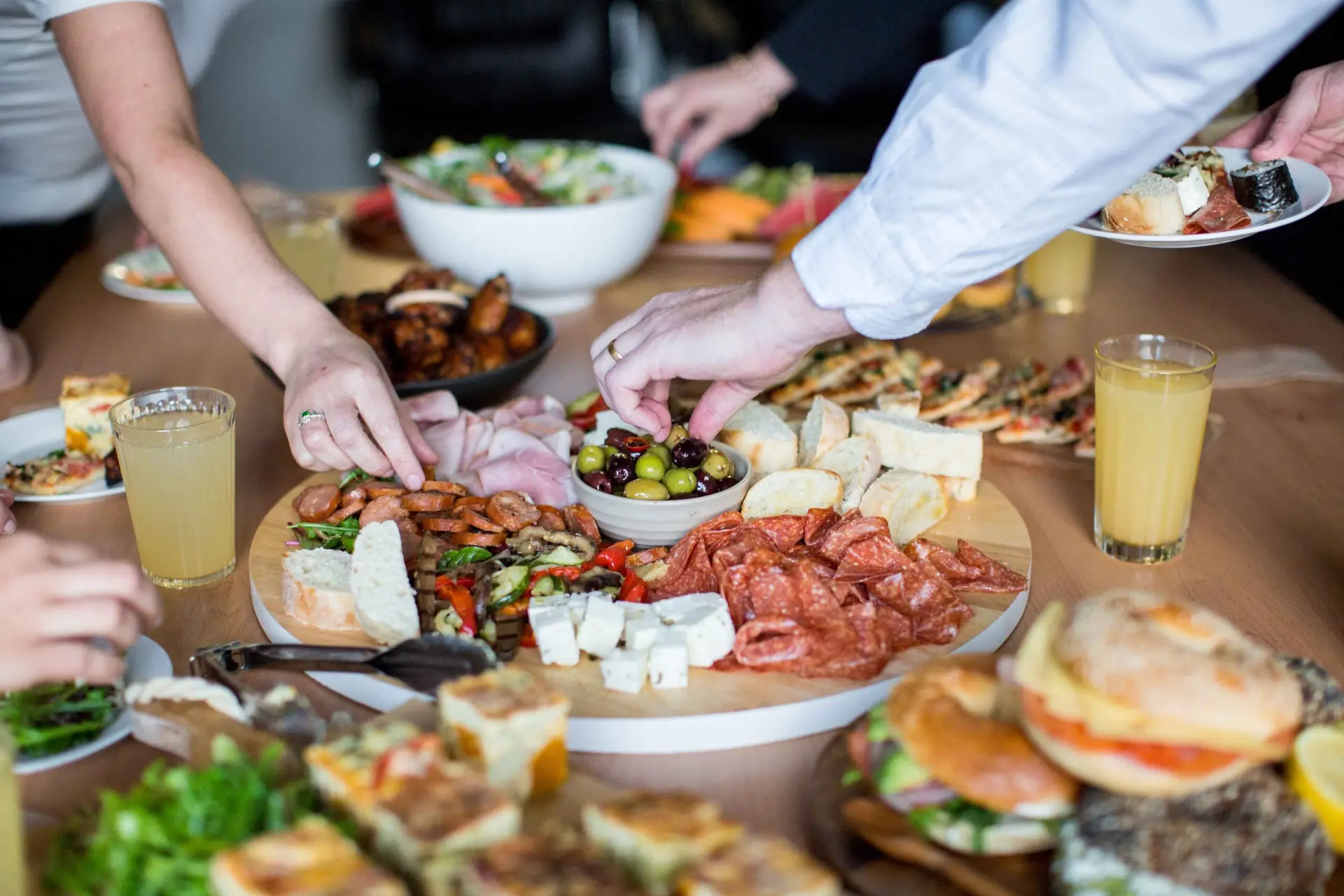 A man's hand reaching from the right corner of the image to pick up an olive from a grazing board