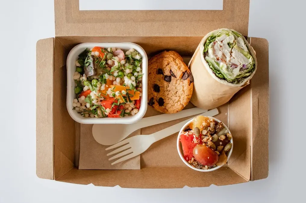 Lunch box with a granola bowl, wrap, cookie and salad.